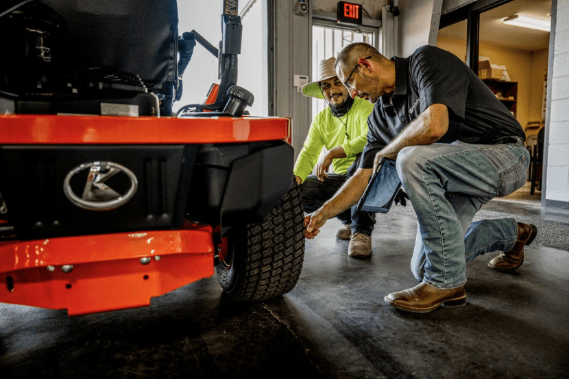 Two men are looking at a zero-turn mower